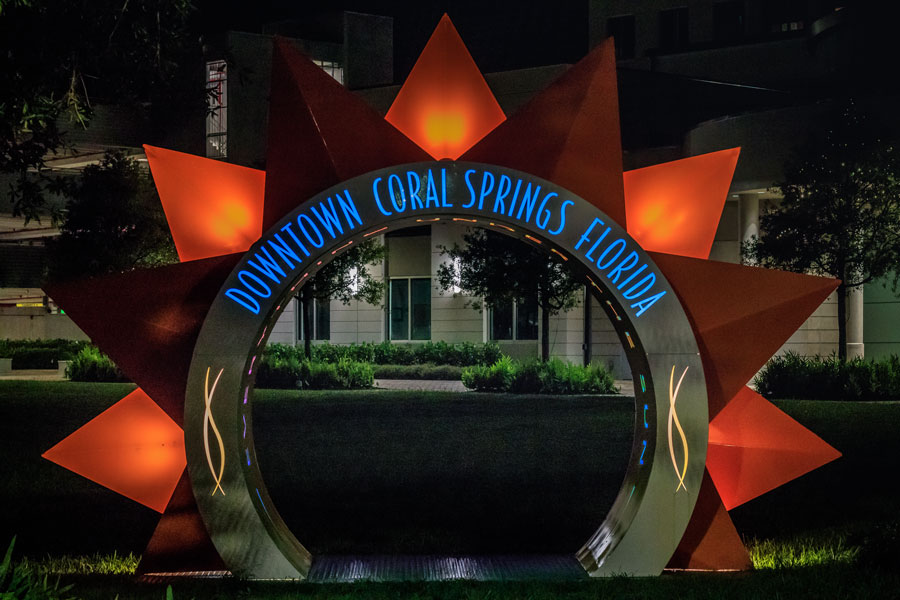 The City Coral Springs Symbol and Sign with City Hall behind at night time. 